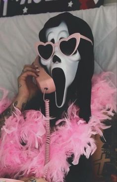 a woman with pink feathers on her head and wearing a mask while talking on the phone