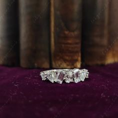 three stone ring sitting on top of a purple velvet covered table next to an old book