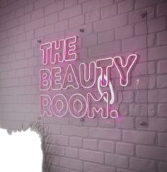 the beauty room neon sign against a brick wall