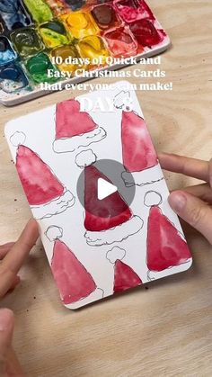 someone is making a christmas card with watercolors and glue on the paper to make it look like santa hats