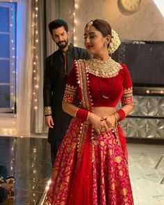 a man standing next to a woman in a red lehenga