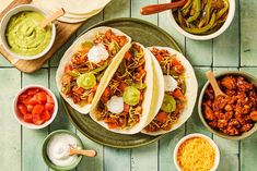 three tacos with toppings sit on a plate next to bowls of salsa and other condiments