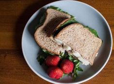 a white plate topped with a cut in half sandwich and strawberries on top of it