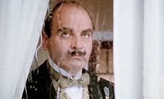 a man in a tuxedo and bow tie looking out the window with white curtains