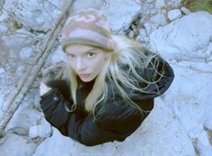 a woman with blonde hair wearing a black jacket and a pink hat is standing on some rocks