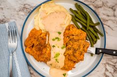 a white plate topped with meat and mashed potatoes covered in gravy next to green beans