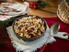 a bowl filled with rice and vegetables on top of a red table cloth next to silverware