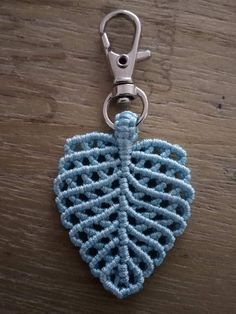 a blue crocheted leaf keychain hanging on a wooden table next to a pair of scissors