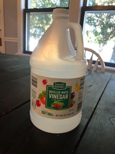 a gallon of white vinegar sitting on top of a wooden table next to a window