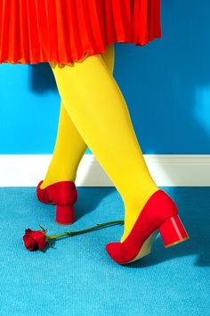 a woman's legs in yellow and red shoes with a flower on the floor