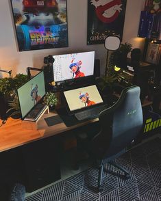 a computer desk with two monitors and a laptop on it in front of some posters