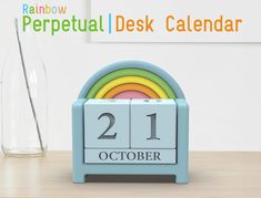 a desk calendar sitting on top of a wooden table next to a vase with a rainbow in it