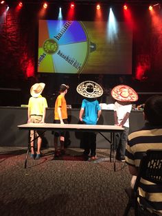 four children standing at a table with paper plates on it in front of a projector screen