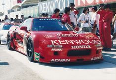 a group of people standing around a red race car in front of a crowd on the street