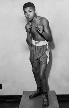 a black and white photo of a young man wearing boxing shorts, standing on a platform