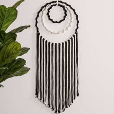 a black and white wall hanging with three necklaces on it next to a potted plant