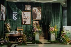 an arrangement of flowers and pictures in front of a green curtained wall with photos on it