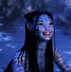 a woman with blue makeup and long black hair smiles at the camera while standing in water