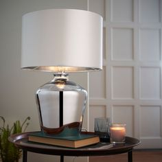 a table lamp sitting on top of a wooden table next to a book and candle