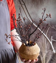 a person holding a vase with branches in it