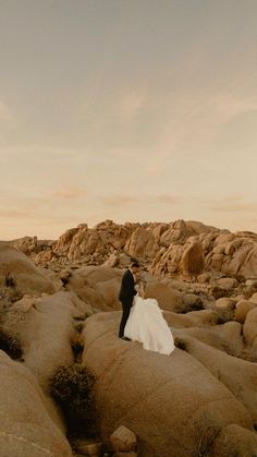 a bride and groom are standing on rocks in the desert at sunset, with their arms around each other