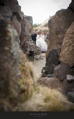 a bride and groom walking through some rocks