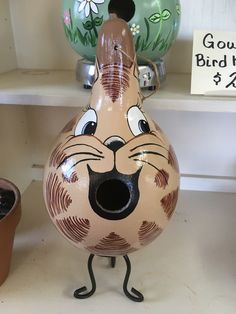 a ceramic vase with a cat face painted on it's body and legs, standing in front of two flower pots