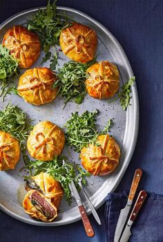 several small pastries on a plate with green garnishes and silverware