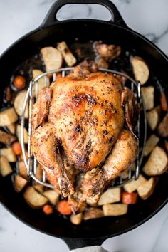 a chicken is cooking in a skillet with potatoes and carrots on the side