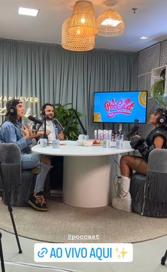 three people sitting around a round table with microphones in front of them, talking to each other