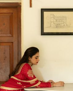 a woman in a red sari sitting at a table and writing on a piece of paper