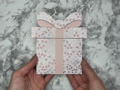 a person holding a pink and white box with a bow on it's side