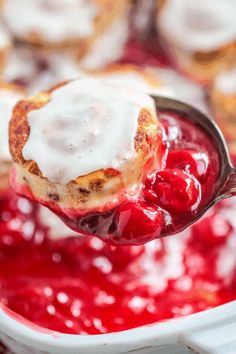 a spoon full of cranberry sauce with cinnamon rolls in the back and on top