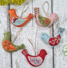 four felt bird ornaments hanging from clothes pins on a white wooden surface with flowers in the background