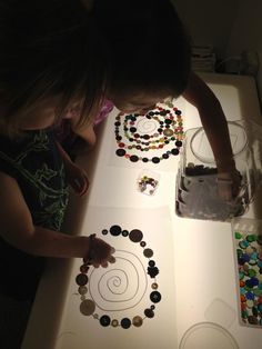 two children are making beaded necklaces at a table with water and beads on it