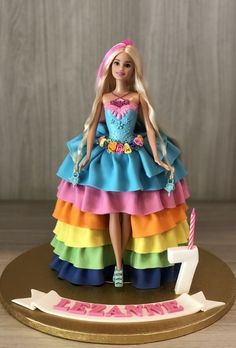 a barbie doll cake with the number one on it's base and rainbow tiered dress