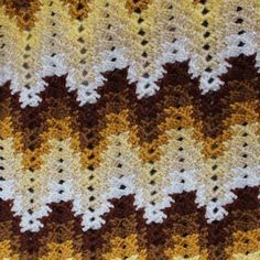 a crocheted blanket with white and brown designs on the bottom, along with an orange border