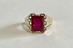 Handsome vintage 10k yellow gold 1940s era ring featuring a vibrant created ruby! The deep red gem weighs an estimated 6 carats, is emerald cut, and securely bezel set. The substantial setting is detailed with a decorative design on the shoulders. Charming vintage piece of fine jewelry for him or her, featuring July's birthstone! ERA - Circa 1950 METAL / MATERIAL - 10k yellow gold, 1 created ruby (estimated 6 carats) [Synthetic ruby contains essentially the same chemical composition & properties Antique Red 14k Gold Signet Ring, Antique Red Signet Ring In 14k Gold, Vintage Ruby Rings With Polished Finish, Classic 14k Gold Red Signet Ring, Classic Red 14k Gold Signet Ring, Classic Red Signet Ring Stamped 14k, Classic Ruby Signet Ring, Vintage 14k Gold Ruby Ring With Polished Finish, Classic Red Sapphire Ring In 14k Gold