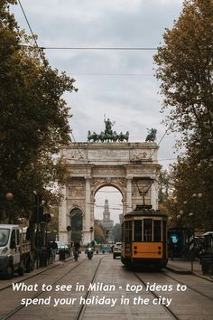 a yellow trolley car driving down a street next to a tall arch with statues on top