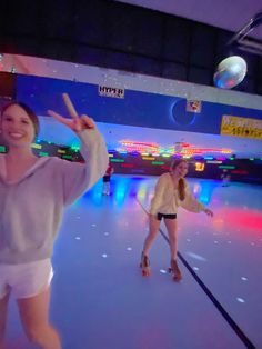 two women in white shorts are skating on an indoor ice rink with lights and disco balls behind them