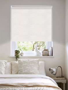 a bedroom with white walls and a large window covered in roman blind shades, along with an unmade bed