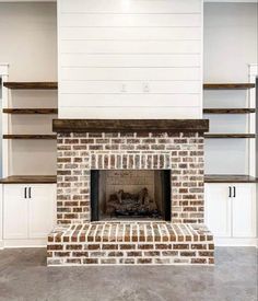 an empty living room with a brick fireplace and white shelving on either side of the fire place