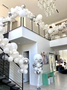 white and silver balloons are hanging from the ceiling in front of a staircase leading up to a second floor