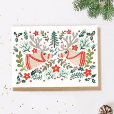 a christmas card with two reindeers and holly leaves on the front, surrounded by pine branches