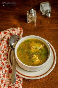 a white bowl filled with green soup on top of a wooden table next to a spoon