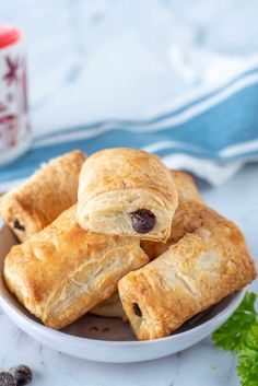 several pastries are on a plate with some parsley next to it and a cup of coffee in the background