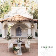 a table set up with flowers and greenery in front of an outdoor gazebo