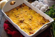 a casserole dish with eggs and other ingredients in the background on a wooden table