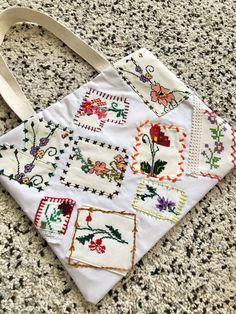 a white bag with embroidered designs on it sitting on the floor next to a carpet