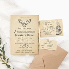 an old baby shower book and envelope on a white blanket with greenery next to it